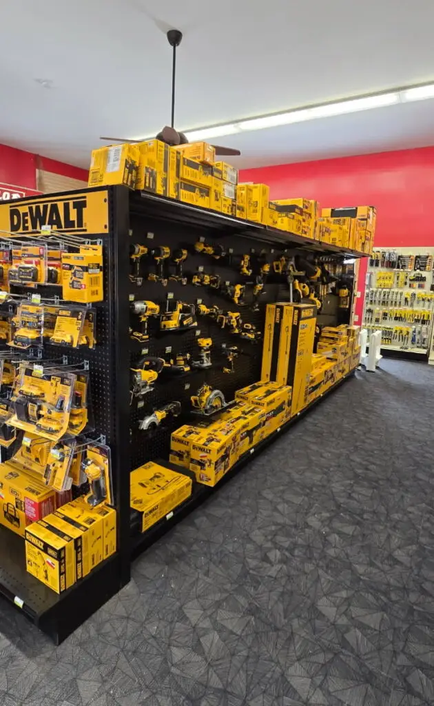 A hardware store display featuring a wide selection of DEWALT power tools and accessories arranged on black shelving with boxed items, mounted tools, and yellow‑and‑black packaging throughout the section.
